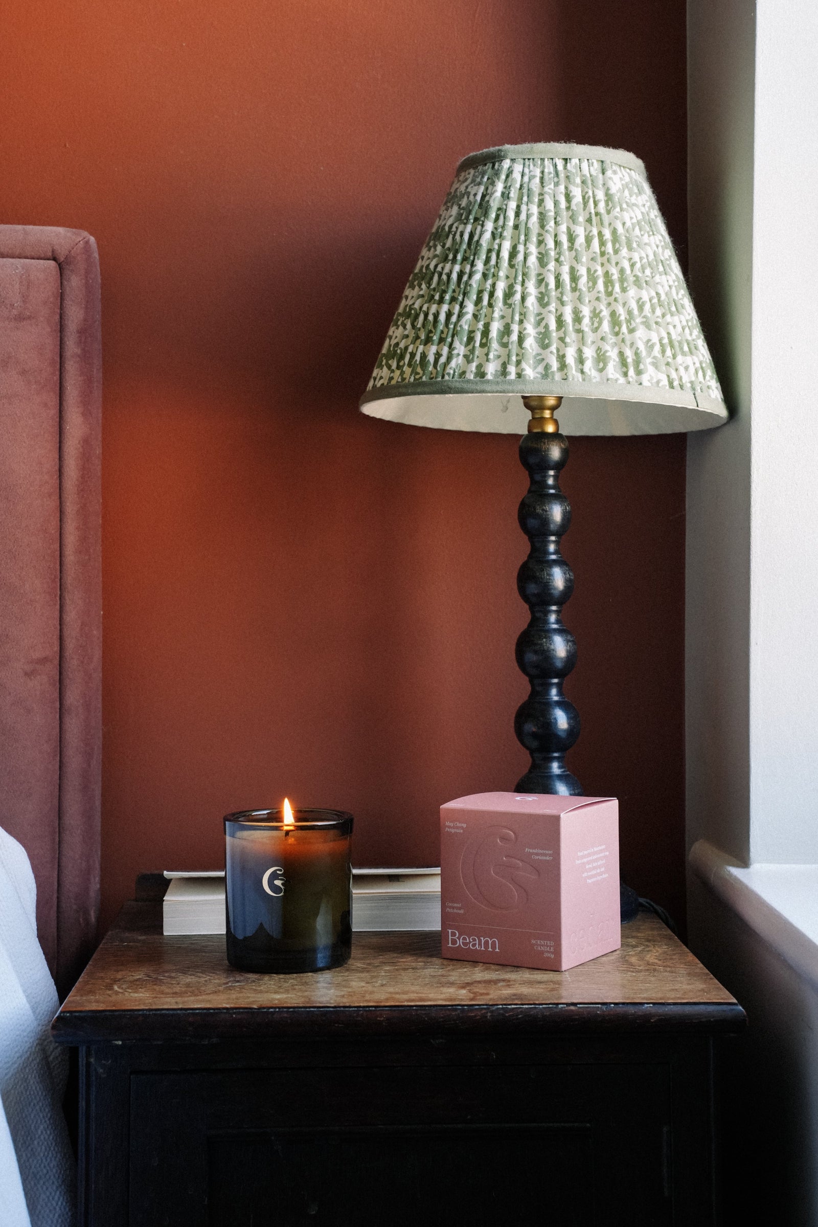 Image of a candle on a bedside table with a green lamp and a box