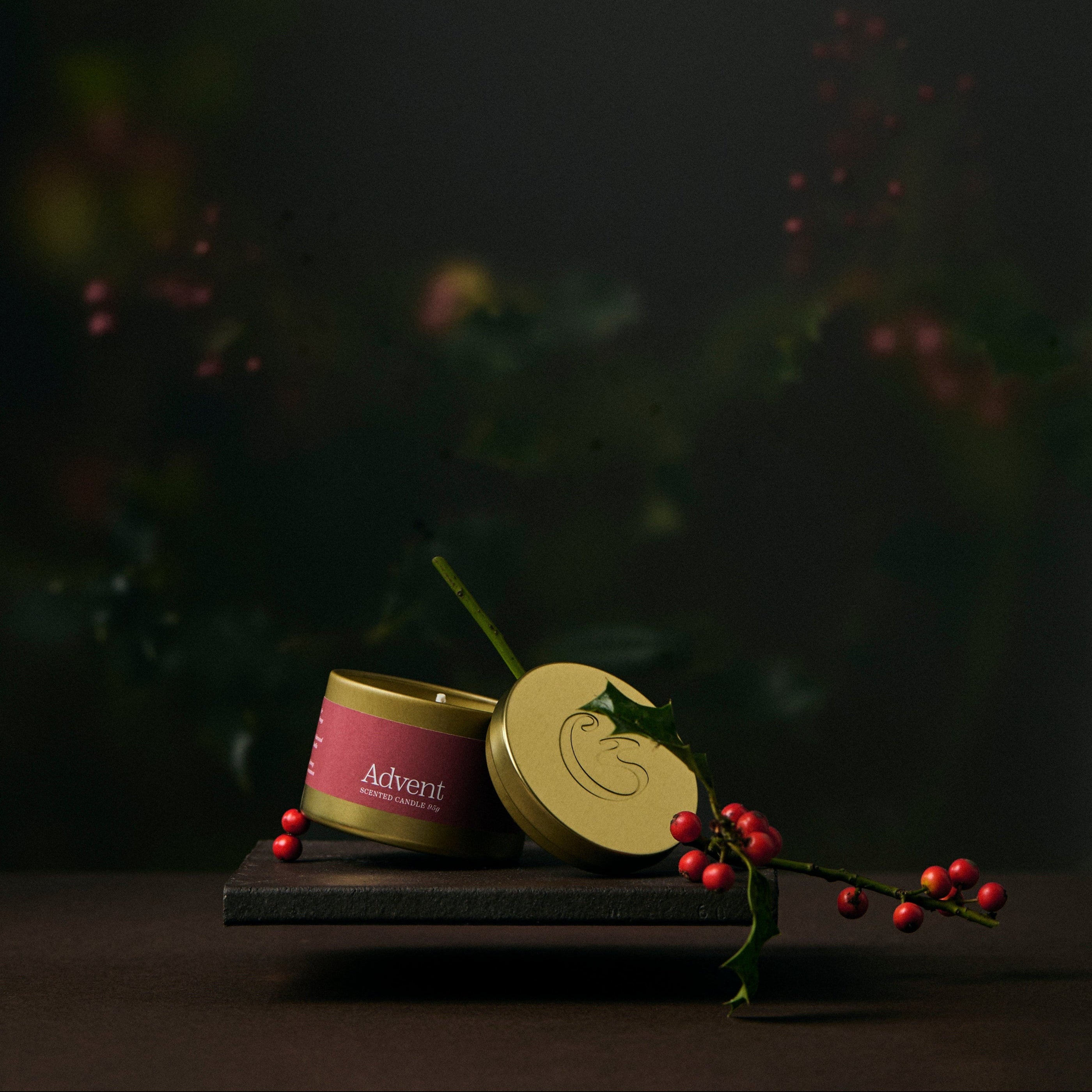 Two gold tin candles on a dark surface with a blurred natural background