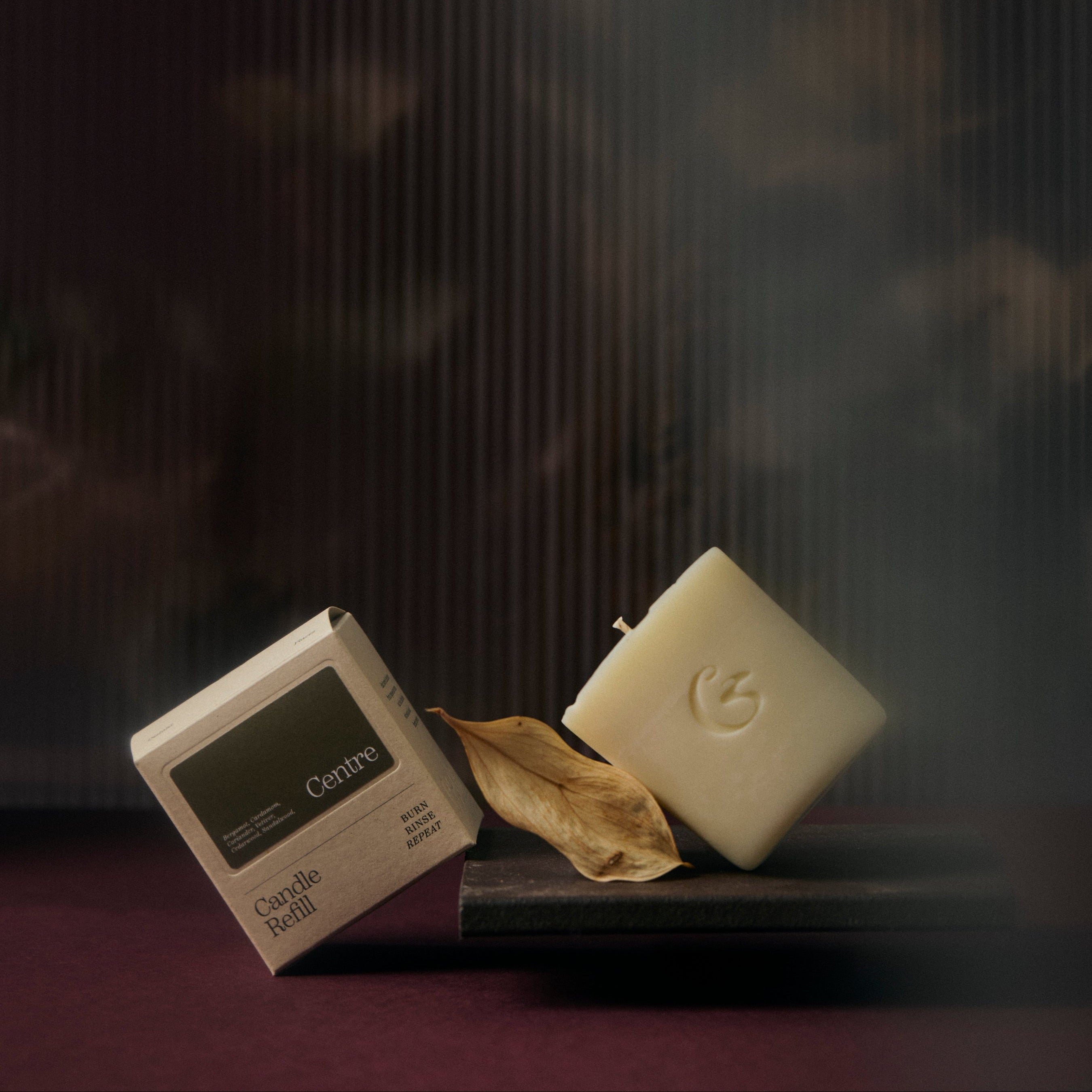 White candle refill with a leaf and packaging on a dark background