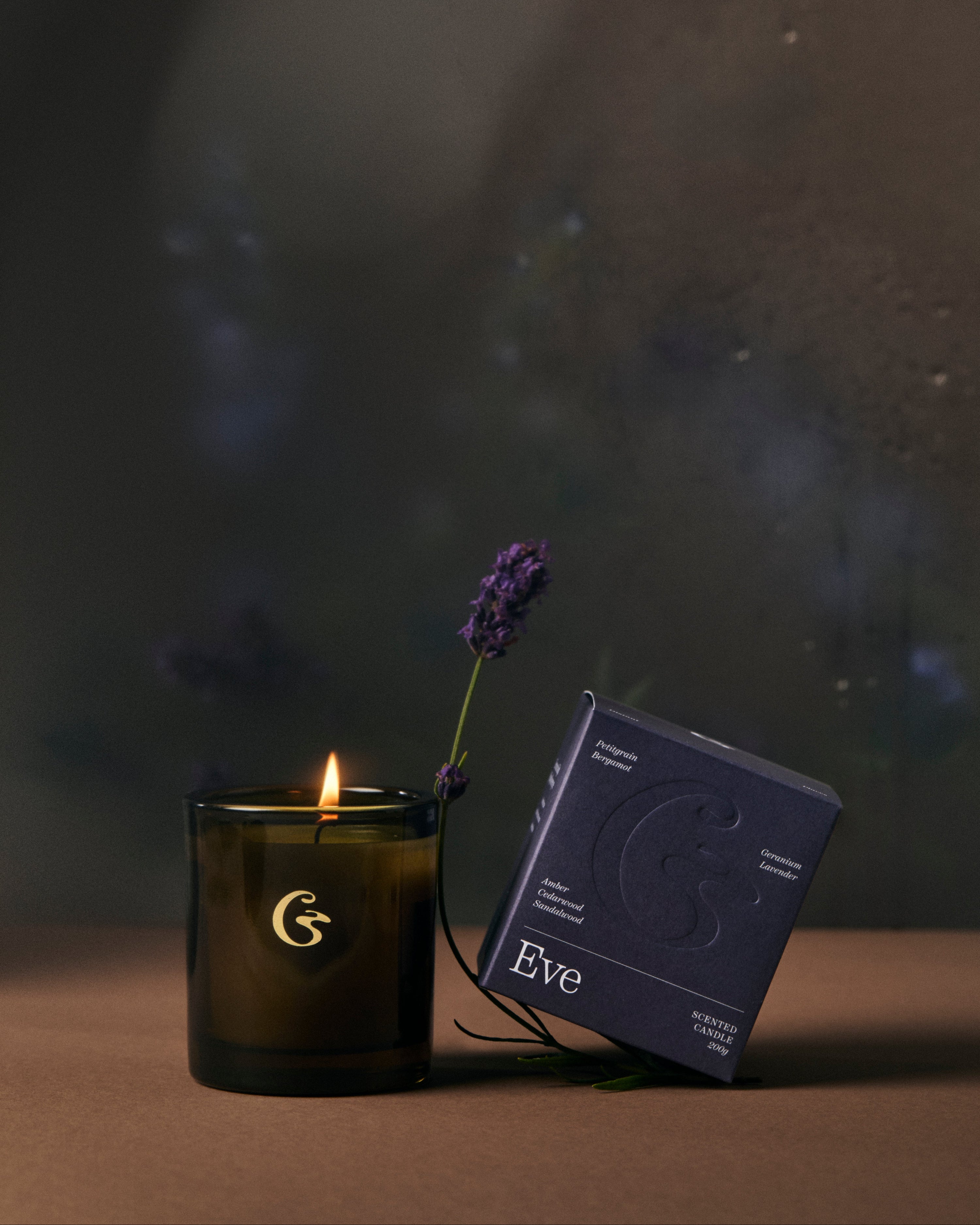 Candle with a lit wick and packaging on a dark background with the name eve