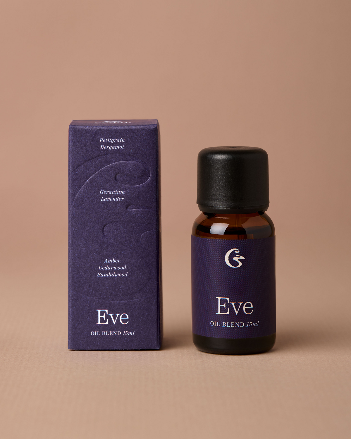 A small amber glass bottle with a black cap stands beside its matching dark purple box on a warm beige studio background. The label and box read Eve and OIL BLEND 15ml.