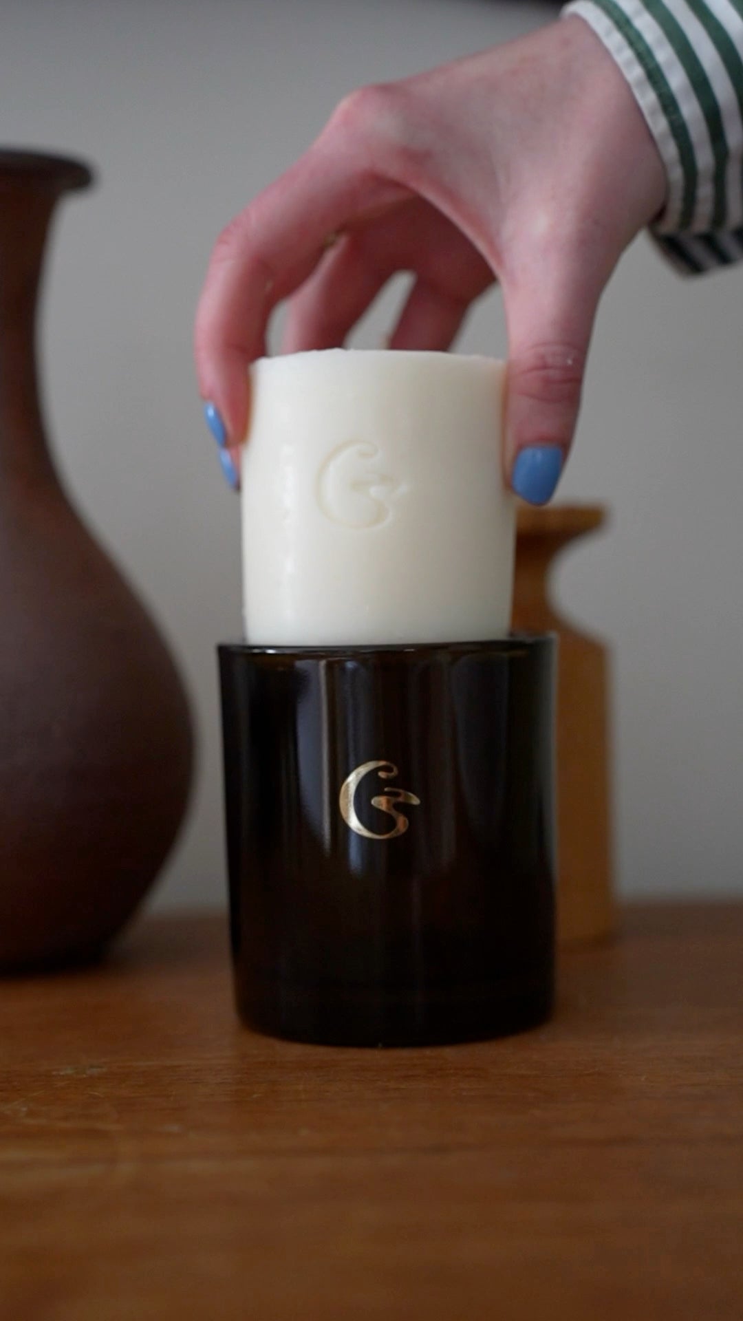 Hand holding a wax candle block with an embossed logo. The wax candle block is about to be inserted in a dark green candle container