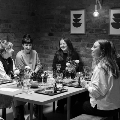 A group of 4 woman sat around a table at a candle workshop. On the table are different bits of equipment