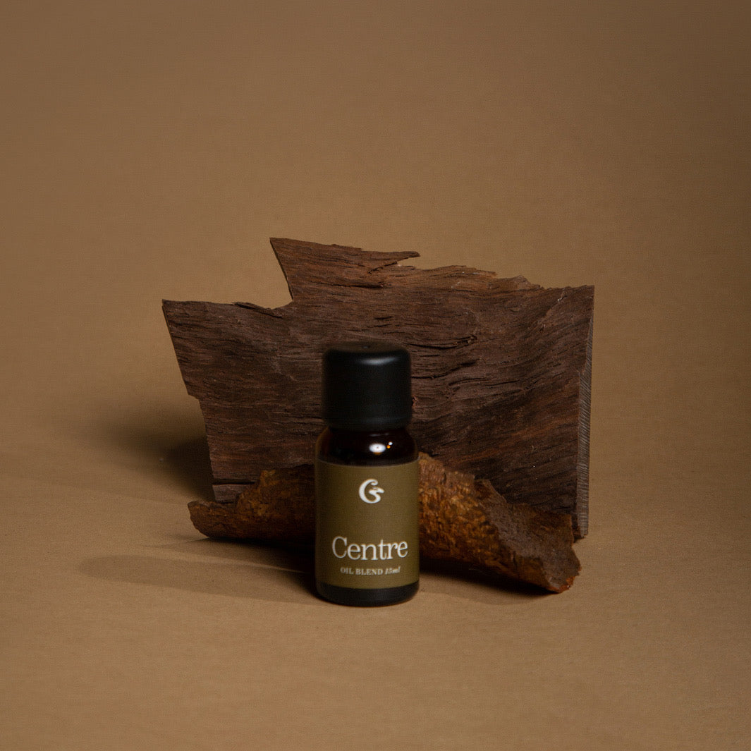 An amber bottle with a black lid and a lable that says Centre Oil Blend 15ml. Sat infront of a piece of wood