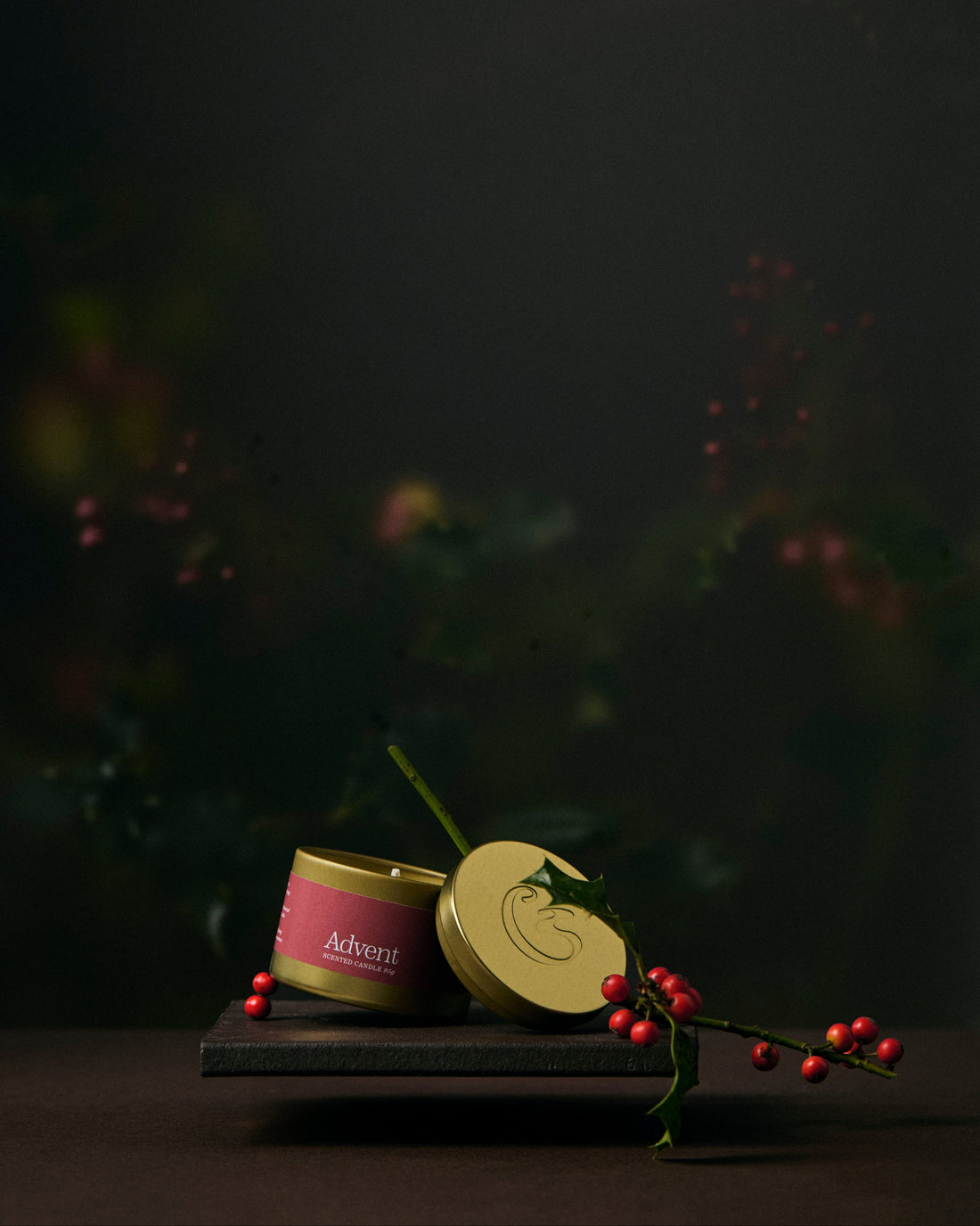 Two gold tin candles on a dark surface with a blurred natural background