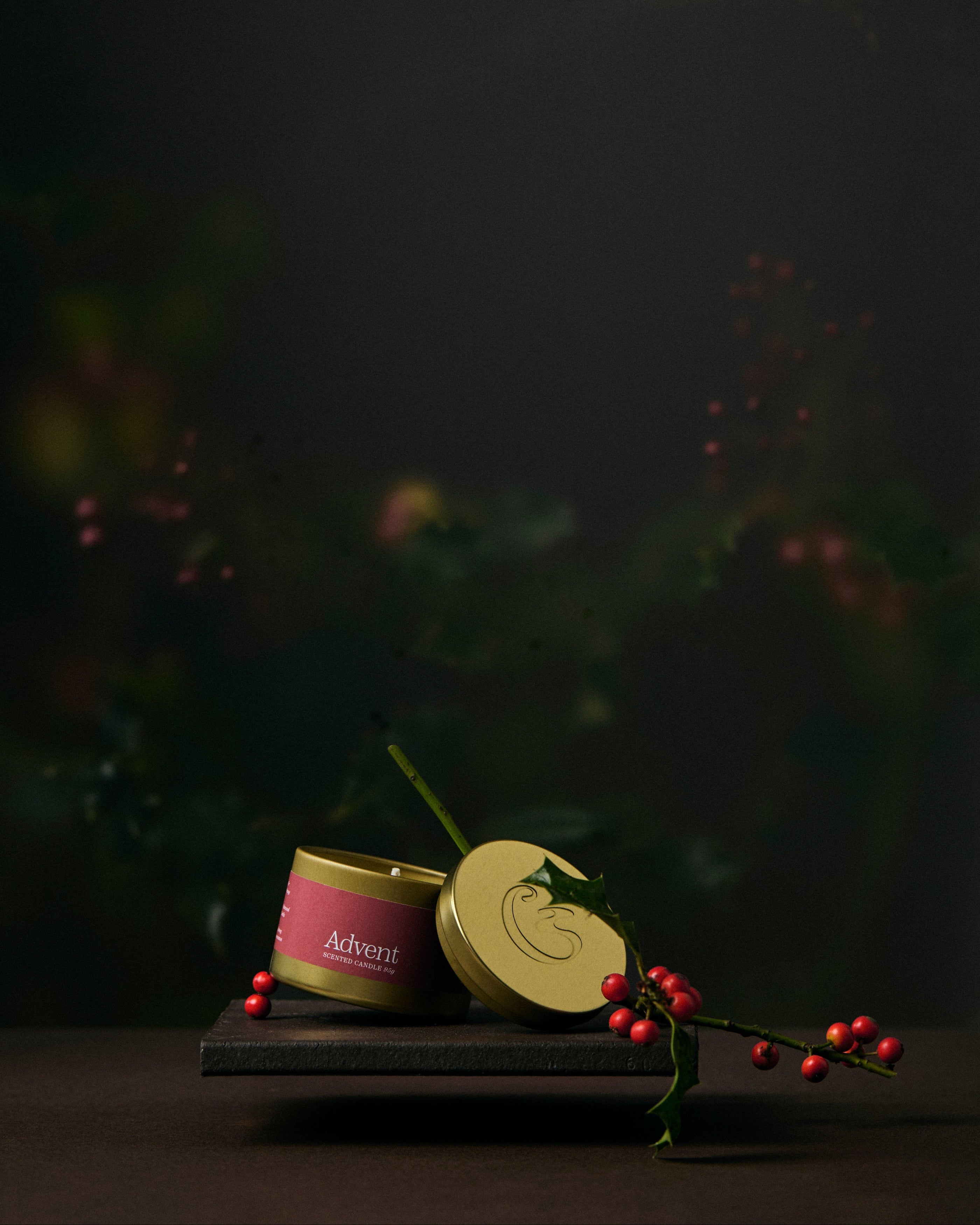 Two gold tin candles on a dark surface with a blurred natural background