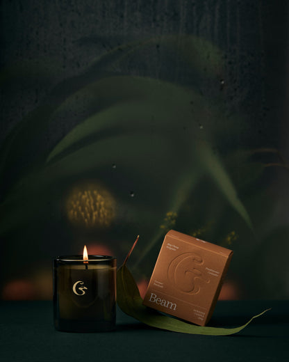 A glass candle lit with an orange box with the name Beam. 