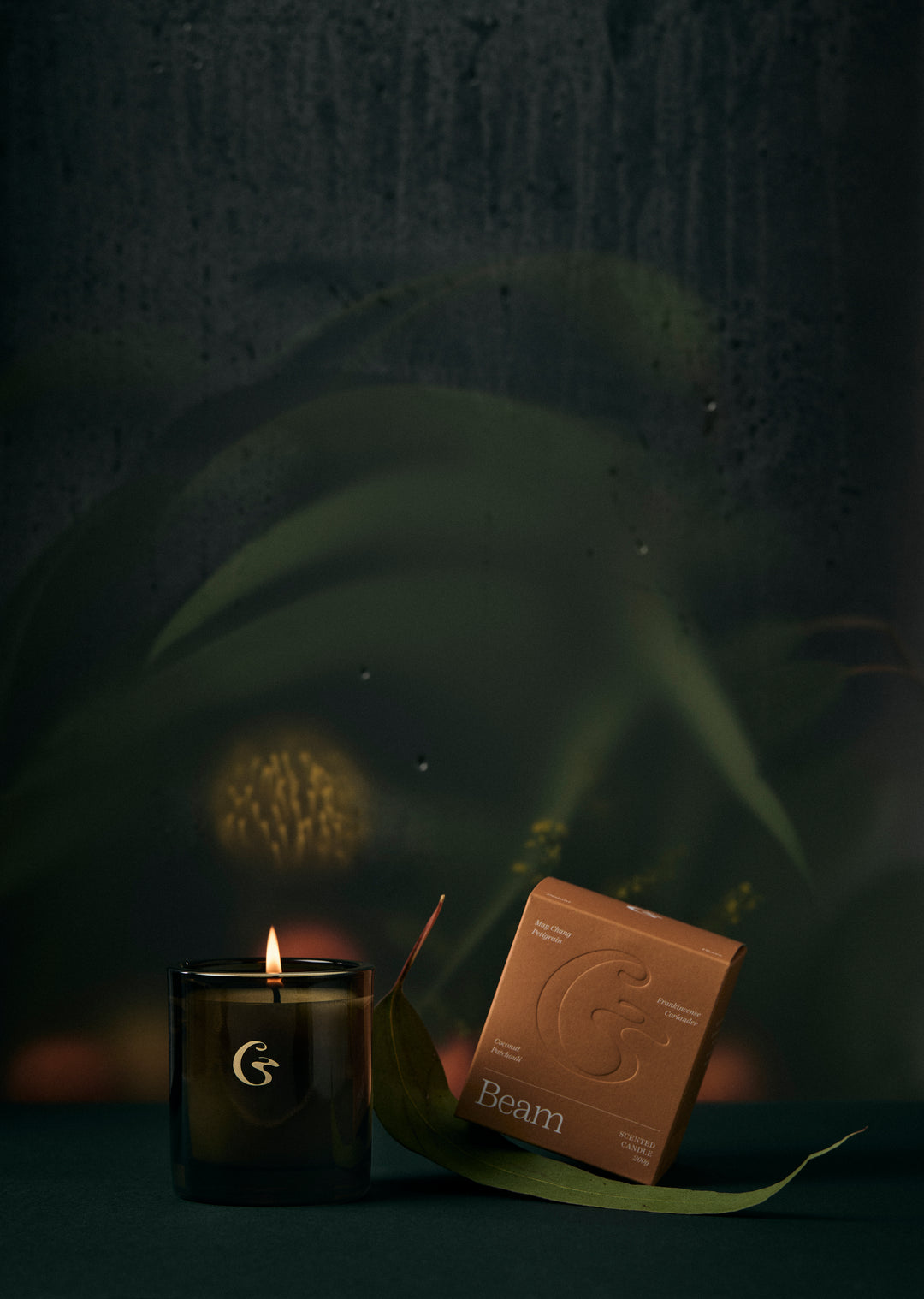 A glass candle lit with an orange box with the name Beam. 