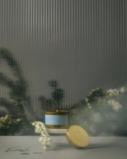 Candle with a decorative label on a reflective surface with blurred plants in the background