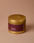 Gold candle jar with a purple label on a beige background